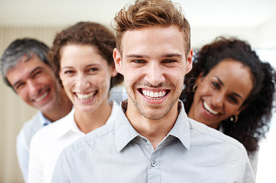 Buy stock photo Closeup portrait of a positive-looking young professional with his coworkers standing behind him