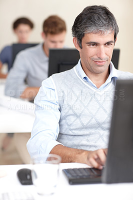 Buy stock photo Shot of an office worker at work on his computer surrounded by colleagues