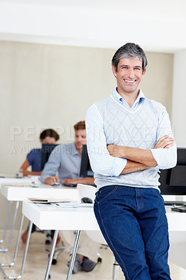 Buy stock photo Portrait of an office manager smiling at the camera with his coworkers sitting behind him