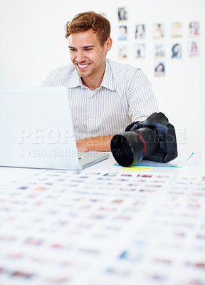 Buy stock photo Smart male photographer sitting at table using laptop and smiling