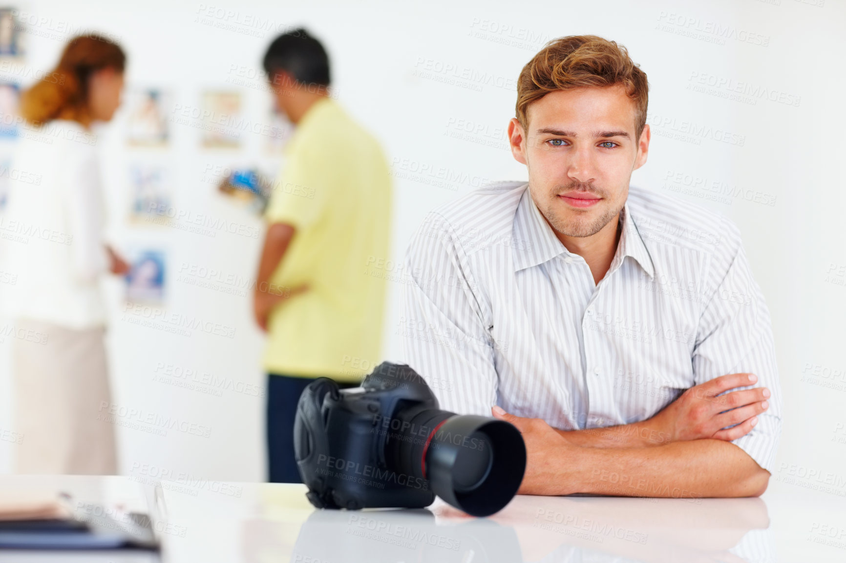 Buy stock photo Portrait of young professional photographer with people looking at images in background