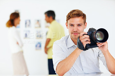 Buy stock photo Portrait of photographer holding camera and smiling with colleagues in background