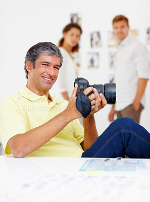 Buy stock photo Portrait of handsome man checking out images in camera and smiling with people in background