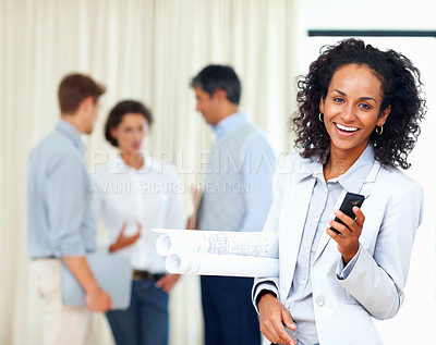Buy stock photo Young female architect holding mobile phone with colleagues discussing in background