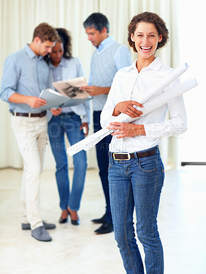 Buy stock photo Laughing business woman holding blueprints with colleagues discussing in background