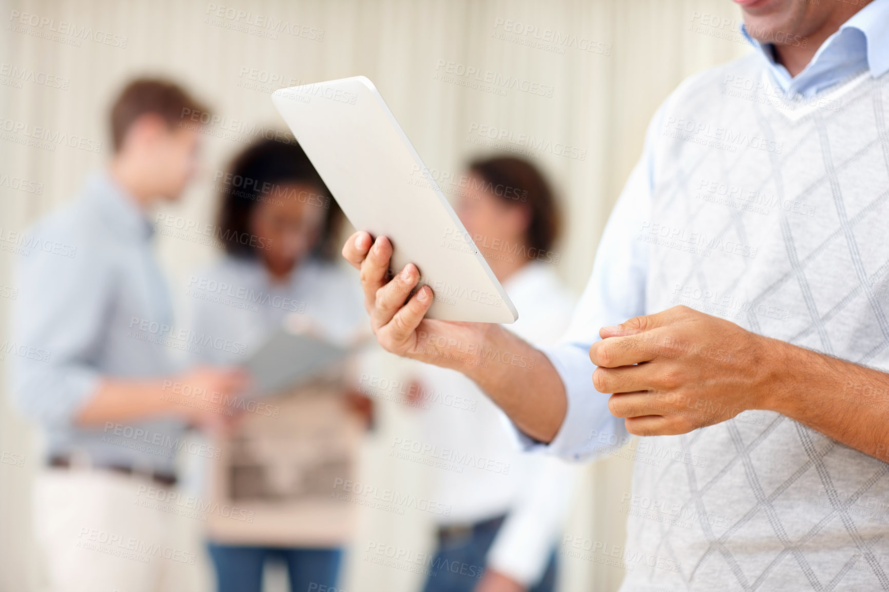 Buy stock photo Business man using tablet PC with colleagues discussing in background