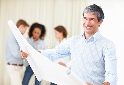 Buy stock photo Smiling business man reading blueprints with colleagues discussing in background