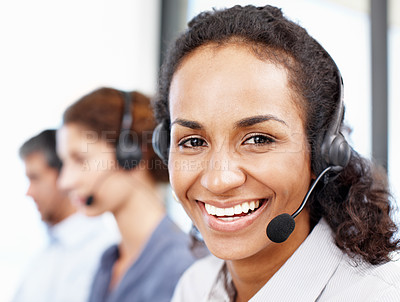 Buy stock photo Closeup portrait of a call center professional working at her computer with colleagues seated in the background