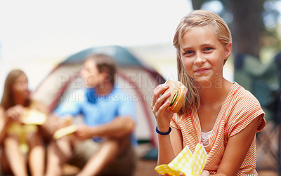 Buy stock photo Portrait of cute young girl eating burger while on a camping holiday with family