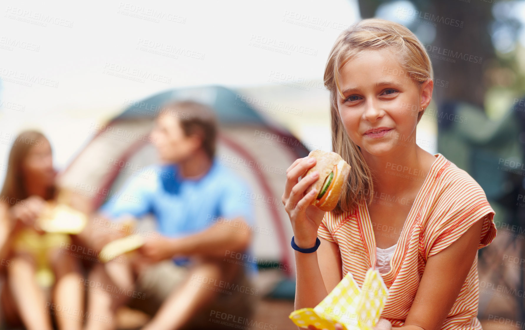 Buy stock photo Portrait of cute young girl eating burger while on a camping holiday with family