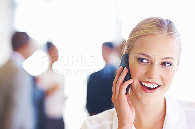 Buy stock photo Closeup of young female executive talking on cellphone with business team in background