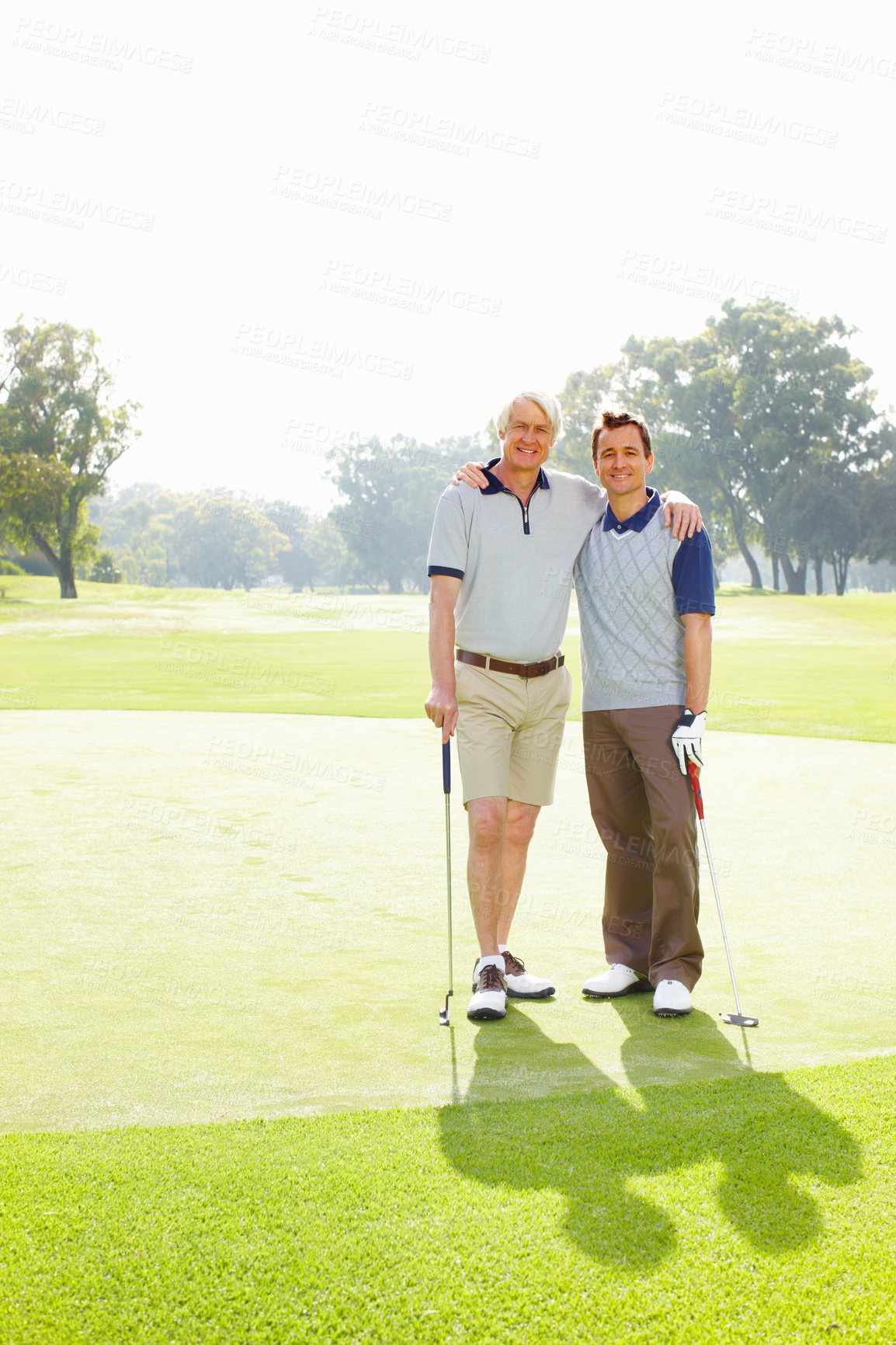 Buy stock photo Full length of father and son standing on golf course with arms around - copyspace