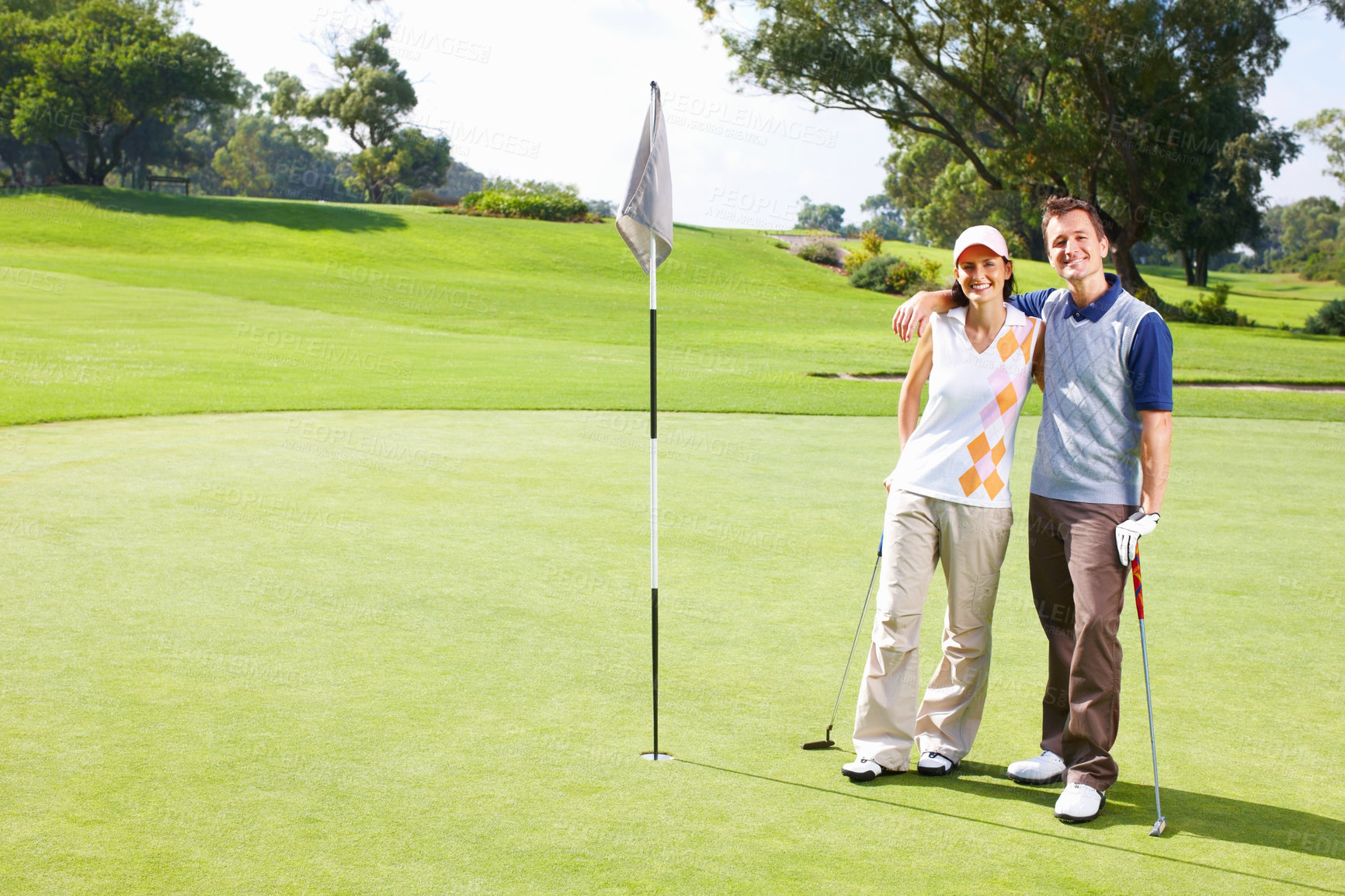 Buy stock photo Full length of golfing couple standing on the putting green with arms around