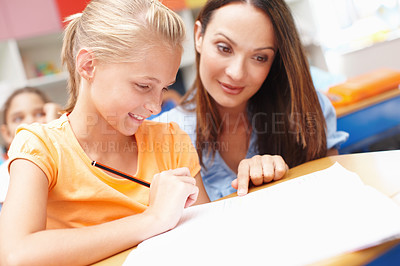 Buy stock photo Teacher, girl and happy with helping in classroom at school for education, teaching and learning. People, educator and smile with student or pupil at in elementary phase for brain development