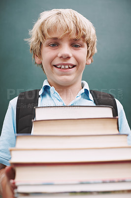 Buy stock photo A cute young boy carrying a large stack of books and smiling at you