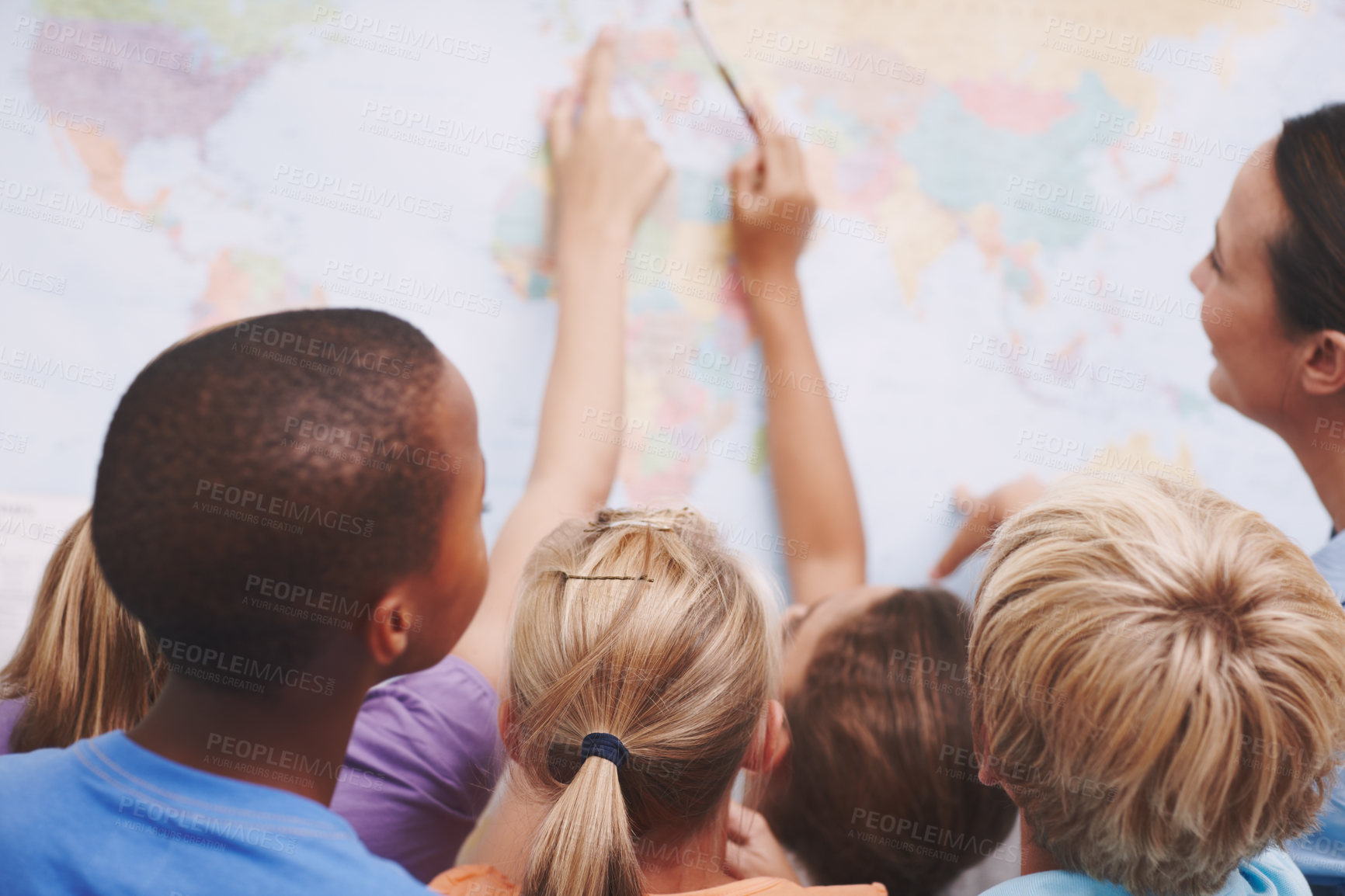 Buy stock photo A group of excited schoolchildren pointing at a world map as their teacher looks on