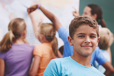 Buy stock photo A cute young boy smiling at you as his classmates and teacher look at a world map in the background