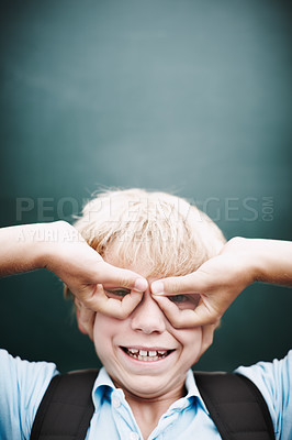 Buy stock photo A funny young boy making glasses with his hands against a classroom blackboard