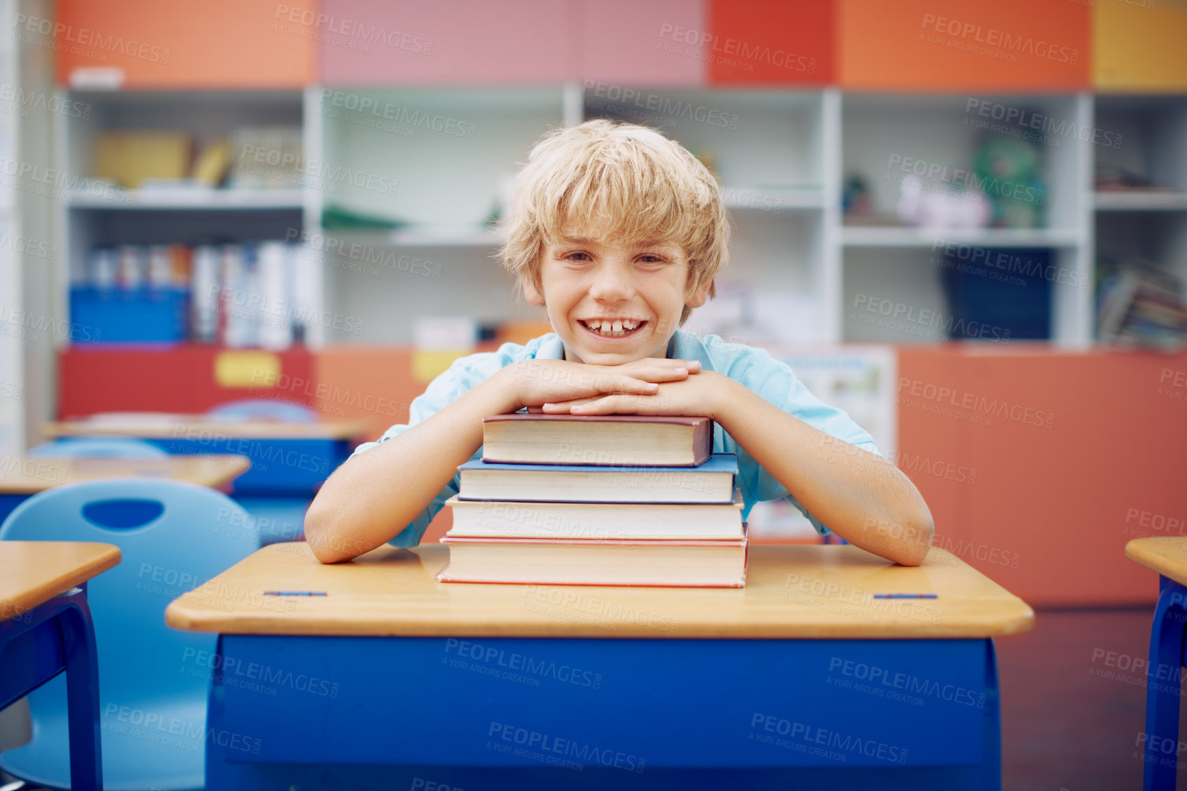 Buy stock photo A happy young boy sitting at his desk and leaning his chin on a stack of books