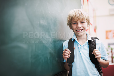 Buy stock photo An happy young boy standing alongside copyspace at the blackboard and holding the straps of his backpack