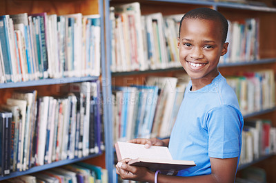 Buy stock photo Black boy, library and smile for reading book at elementary school for literacy, knowledge and information. Student, kid and happy on portrait for education, novel or literature for brain development