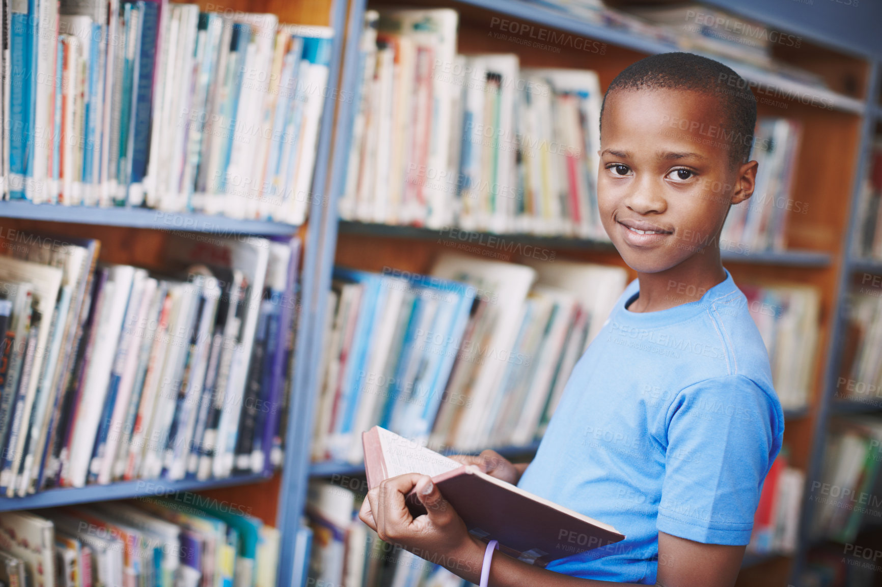 Buy stock photo Black boy, library and happy for reading book at elementary school for literacy, knowledge and information. Student, kid and smile on portrait for education, novel or literature for brain development