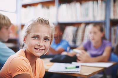 Buy stock photo A pretty young girl sitting in the library with her classmates alongside copyspace