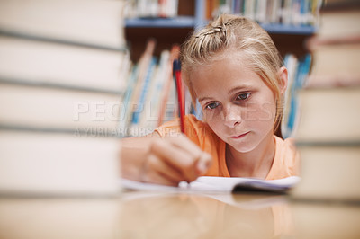 Buy stock photo A cute young girl doing schoolwork while surrounded by books at the library