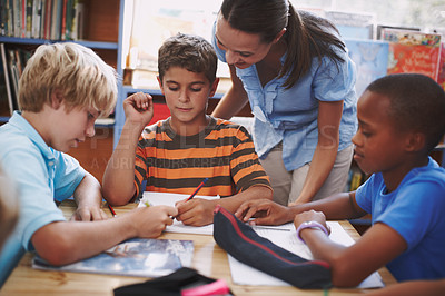 Buy stock photo A pretty young teacher helping her students with their work in the library