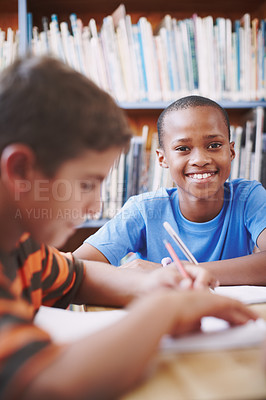 Buy stock photo An african american boy sitting in the library and working with his classmates