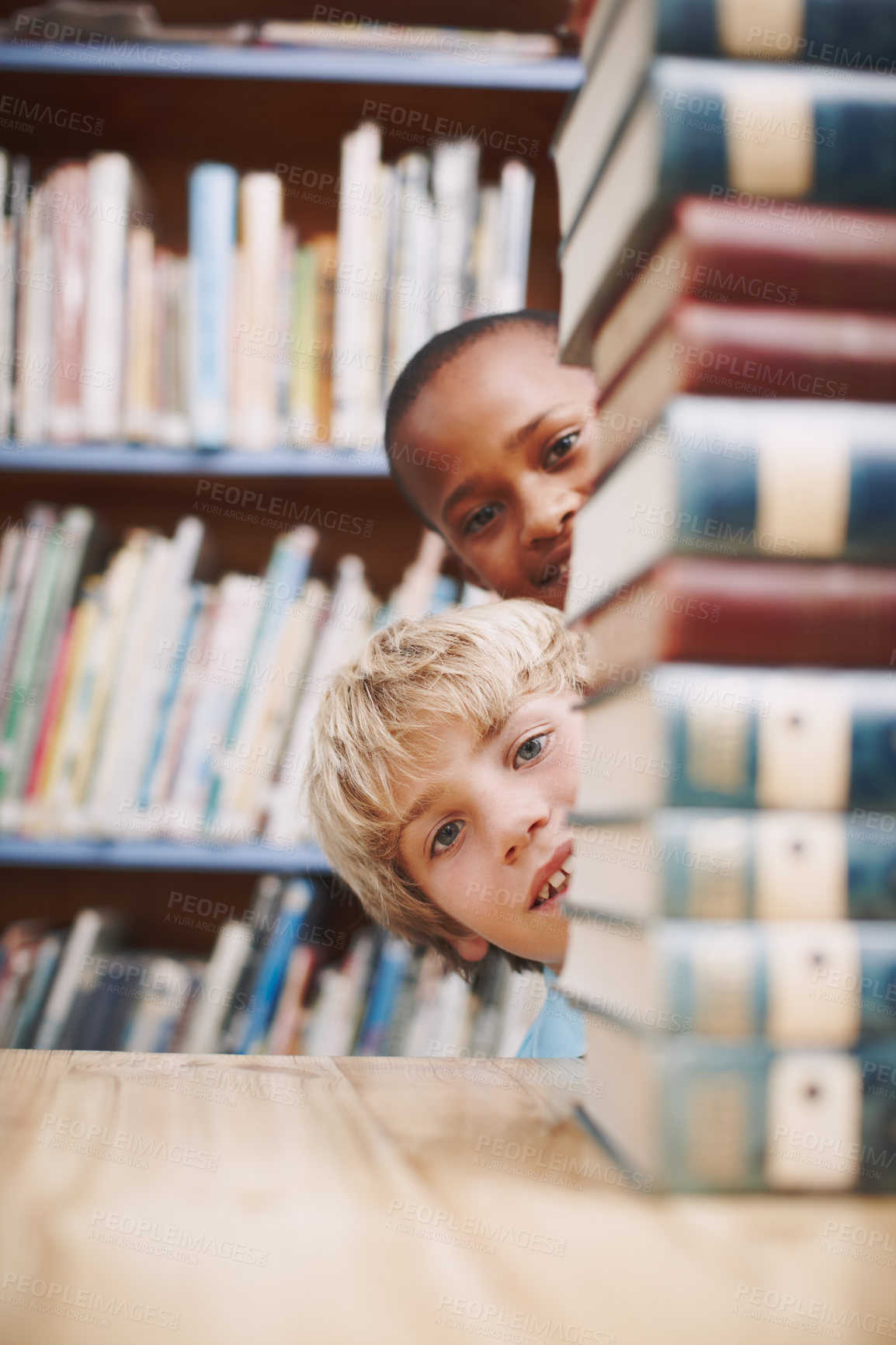 Buy stock photo Boys, portrait and books in library for learning, education and fun with hiding, knowledge and shelf. Student, face and playing in school for development, study and history with academic scholarship 