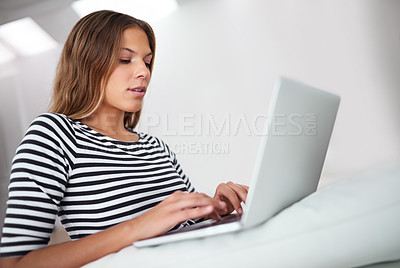 Buy stock photo Shot of a young woman using a laptop while sitting on a sofa at home