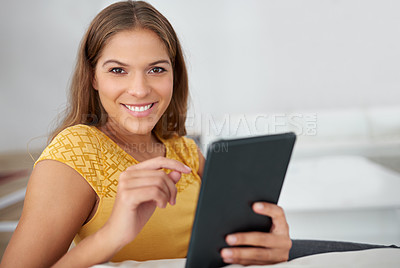 Buy stock photo Portrait of a young woman using a digital tablet while sitting on a sofa at home