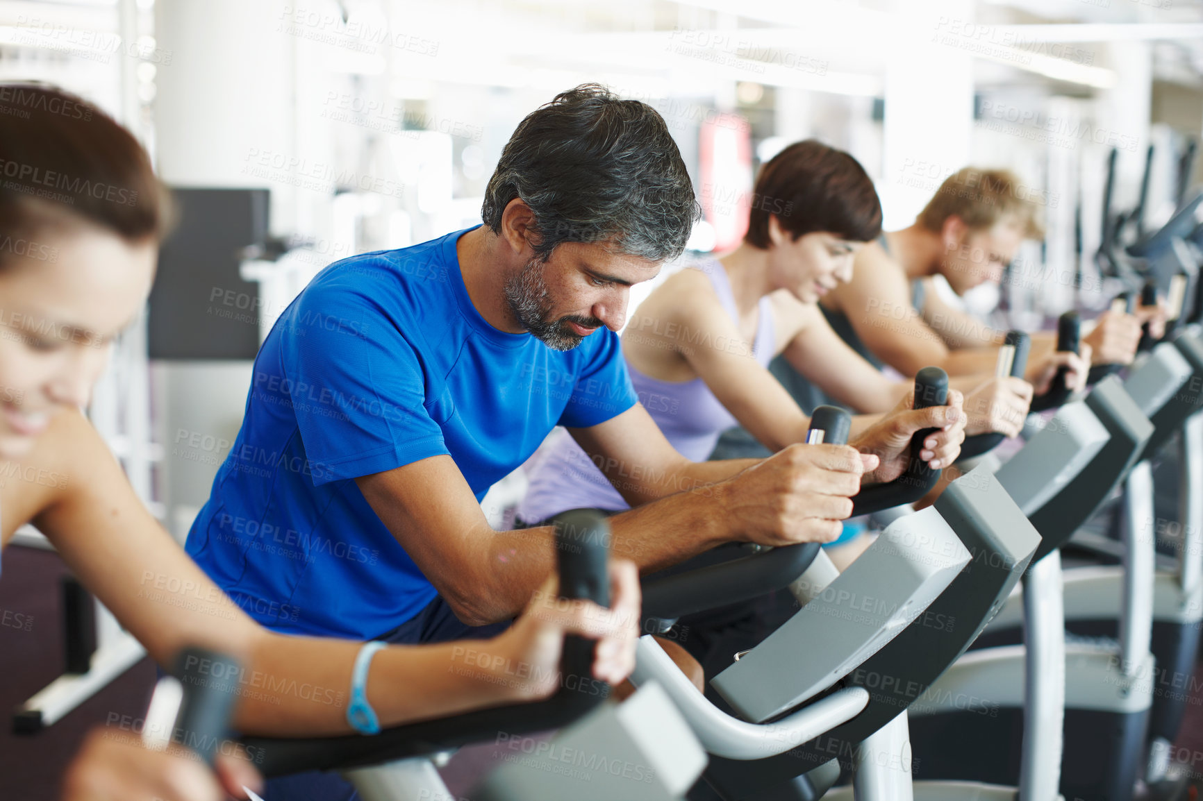 Buy stock photo Cropped shot of a row of people working out on the exercise bikes at the gym