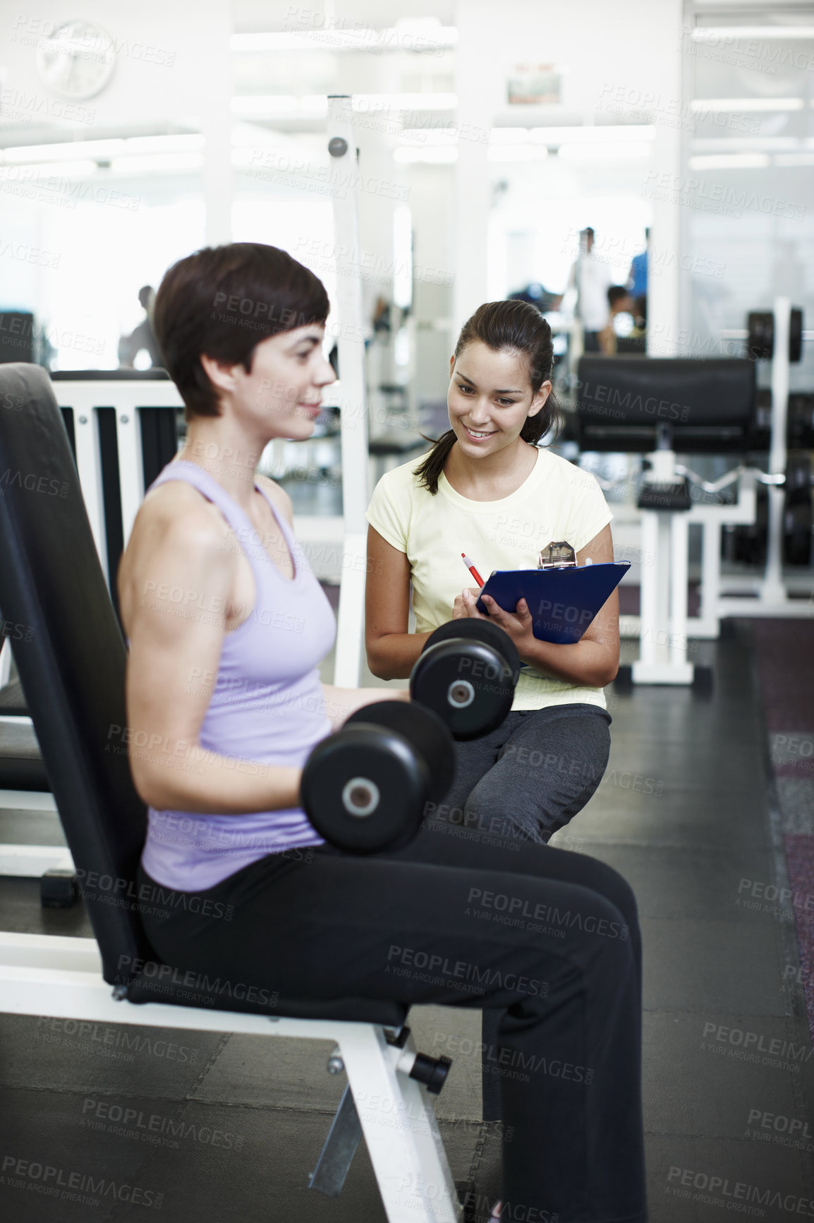 Buy stock photo Cropped shot of an attractive young woman training on the weights with her personal trainer