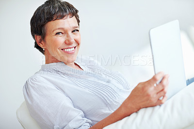 Buy stock photo Portrait of smiling mature woman using tablet PC while sitting on couch