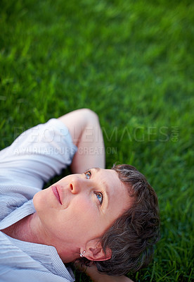 Buy stock photo Thoughtful mature woman relaxing while lying on grass