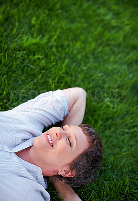 Buy stock photo Relaxed mature female smiling while lying on grass
