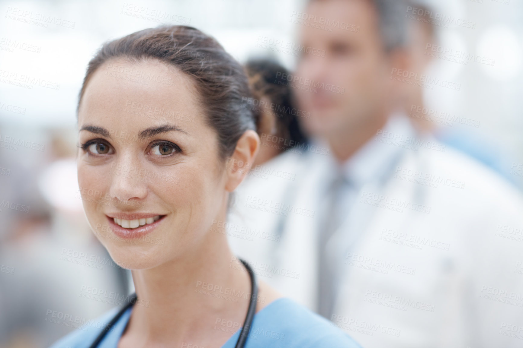 Buy stock photo Young female doctor smiling at the camera with her colleagues in the background