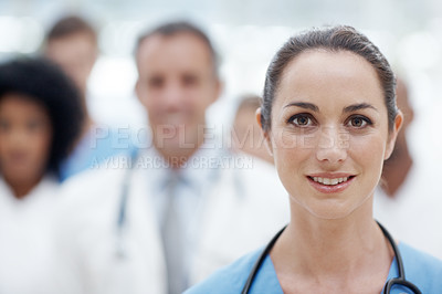 Buy stock photo Happy female doctor smiling at the camera with her colleagues in the background