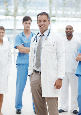 Buy stock photo Mature doctor wearing a labcoat standing in front of his colleagues and smiling - portrait