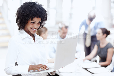 Buy stock photo An african woman using her laptop in the office with her colleagues in the background