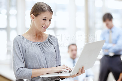 Buy stock photo An attractive young woman using her laptop in the office with her colleagues behind her