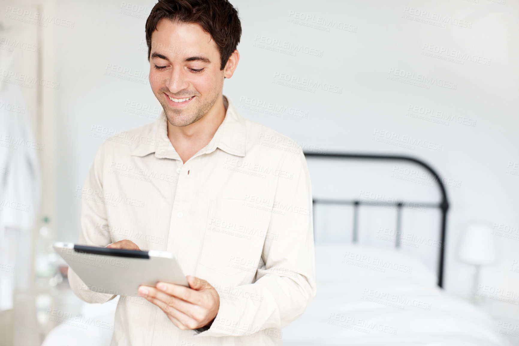 Buy stock photo Happy young man holding his digital tablet and checking his emails while in his bedrrom