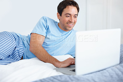 Buy stock photo Relaxed young man lying on his bed as he types on his laptop