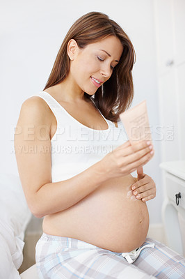 Buy stock photo Happy young pregnant woman applying cream to her stomach