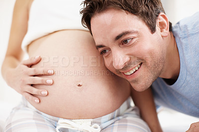 Buy stock photo An excited man listening to his child moving in his wife's stomach