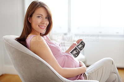 Buy stock photo Portrait of a pretty young woman looking at her babies sonogram while sitting at home