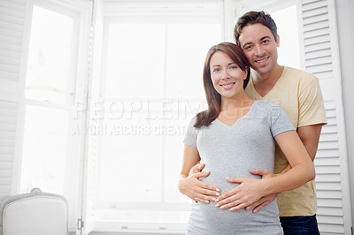 Buy stock photo Proud expecting couple standing together in their living room besides copyspace