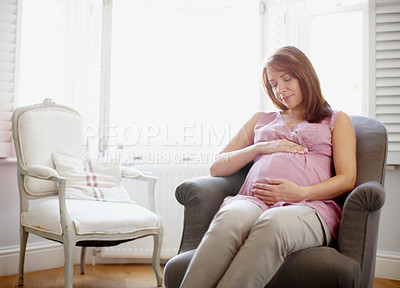 Buy stock photo A glowing pregnant woman looking at her swelling baby bump lovingly - Copyspace